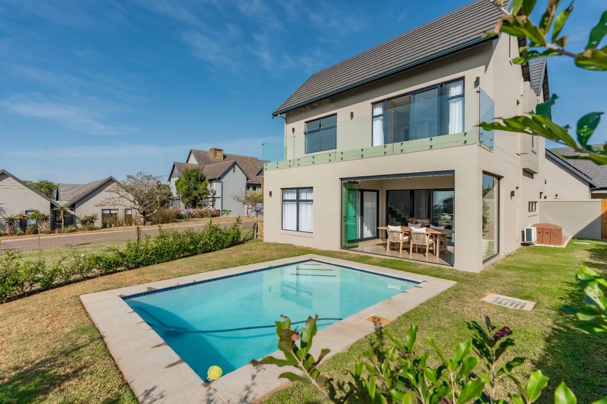 Rear view of a modern two-story house featuring a swimming pool, glass balcony balustrades, and large sliding doors opening to the garden.