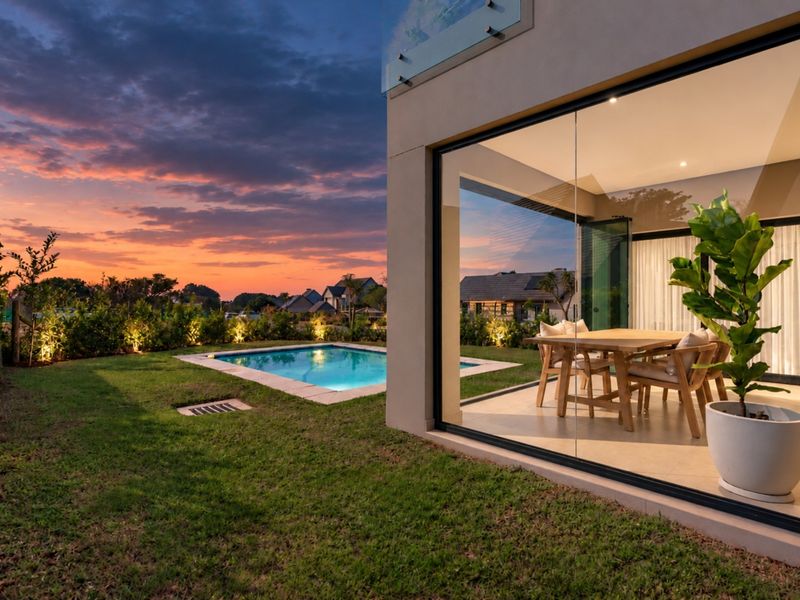 A modern rear exterior view featuring a swimming pool, landscaped garden, and a seamless indoor-outdoor transition through large glass sliding doors.
