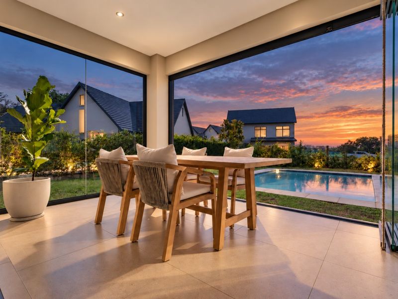 A modern covered patio featuring frameless glass sliding doors that open to a garden and swimming pool area, perfect for indoor-outdoor entertaining.