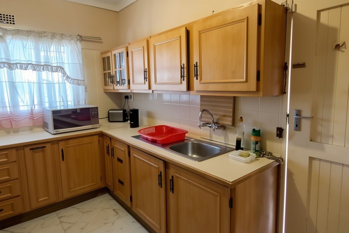 A functional kitchen featuring wooden cabinetry, laminate countertops, a stainless steel sink, and tiled flooring, offering a classic layout with potential for modernization.