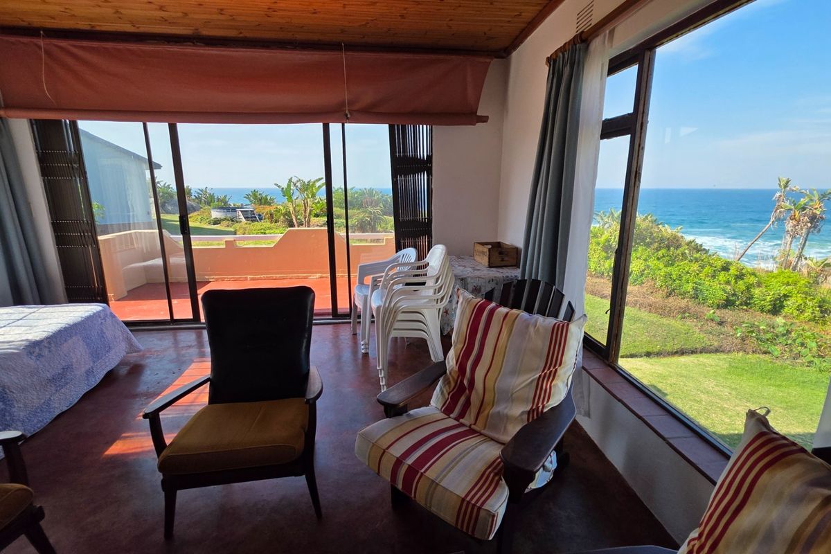 A bedroom featuring timber ceilings and large windows with expansive ocean views, providing direct access to an outdoor patio area.
