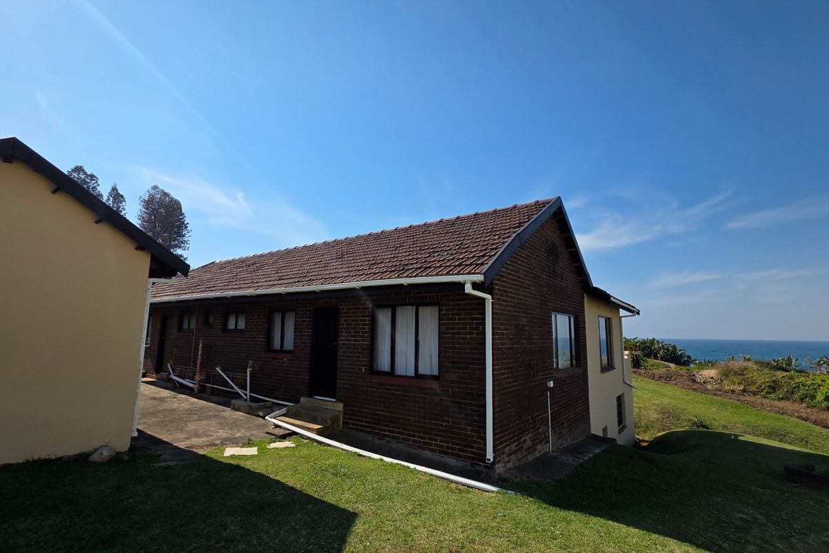 Rear view of a brick-clad house with a tiled roof, featuring a concrete pathway and coastal views in the background.
