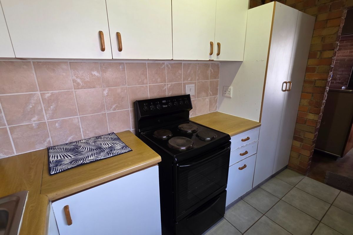 A functional kitchen featuring laminate countertops, white cabinetry, a ceramic tile backsplash, and a freestanding electric stove with tiled flooring.