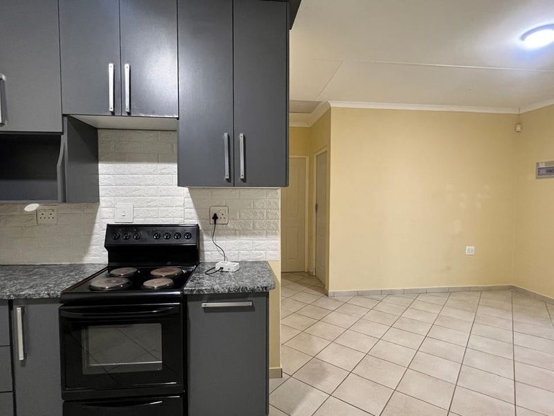 Open-plan kitchen featuring dark grey cabinetry, laminate countertops, and an electric stove, flowing into an adjacent living area with tiled flooring.