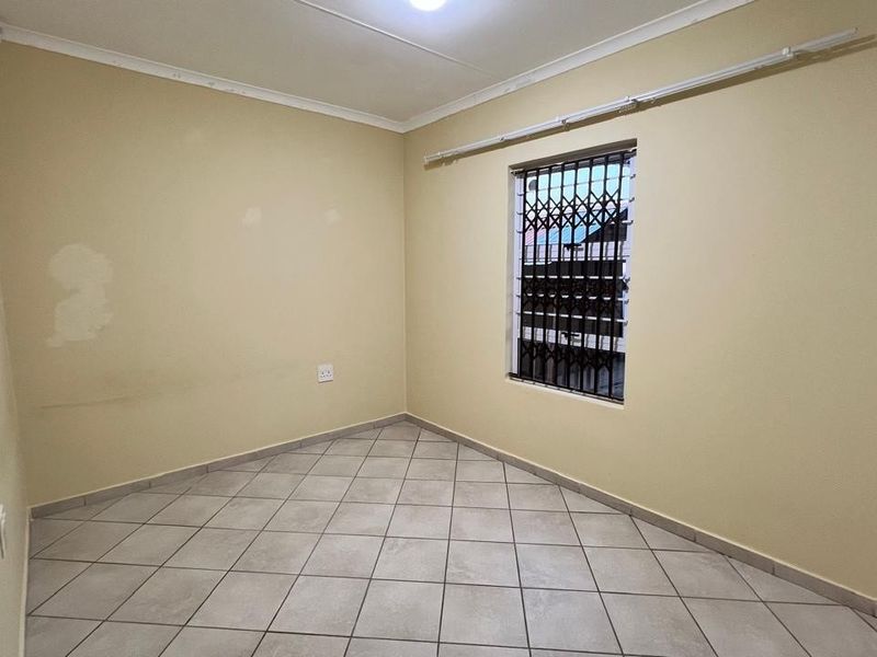 An empty bedroom featuring tiled flooring and a window fitted with security bars, requiring minor cosmetic updates to the wall finishes.