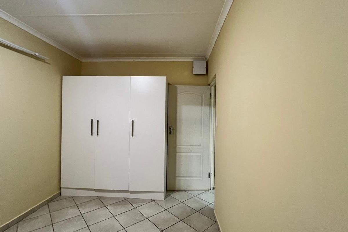A simple bedroom featuring tiled flooring, a built-in white wardrobe, and neutral wall tones, offering a clean and functional space.