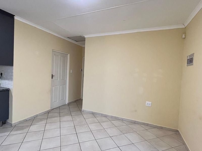 An empty open-plan living area featuring tiled flooring, coved ceilings, and a compact kitchen section with dark cabinetry.