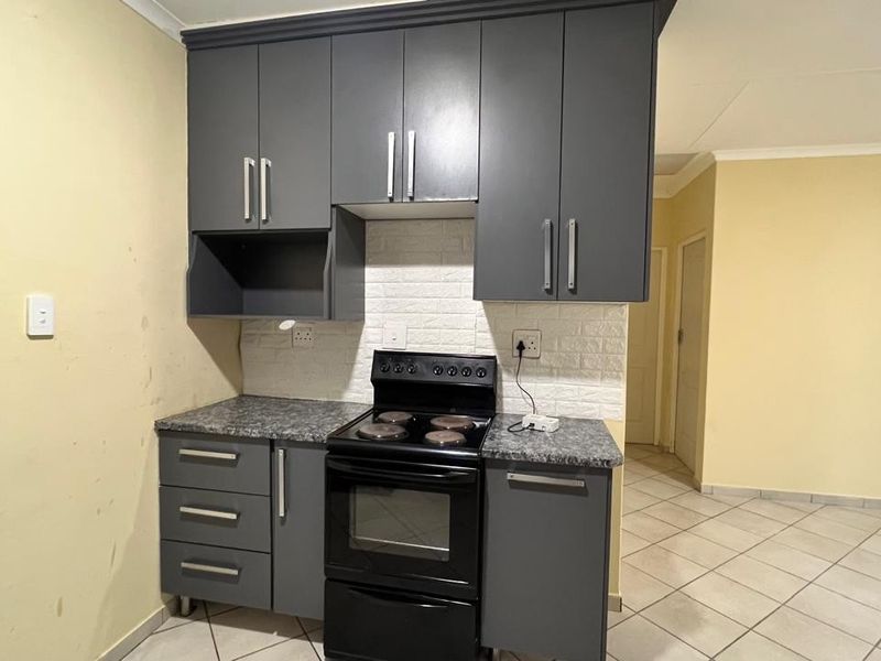 Compact kitchen featuring dark grey cabinetry, a freestanding stove, stone-look laminate countertops, and a textured brick-effect backsplash.