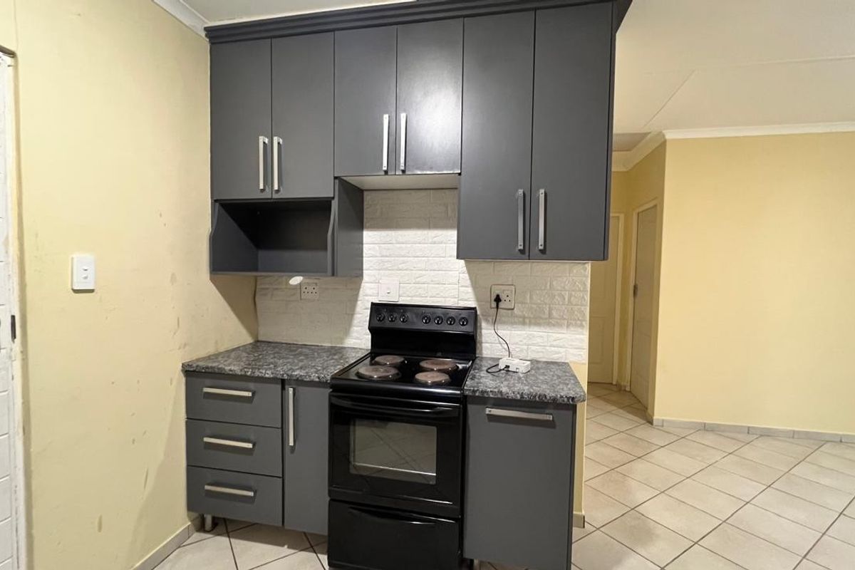 Compact kitchen featuring dark grey cabinetry, a freestanding stove, stone-look laminate countertops, and a textured brick-effect backsplash.