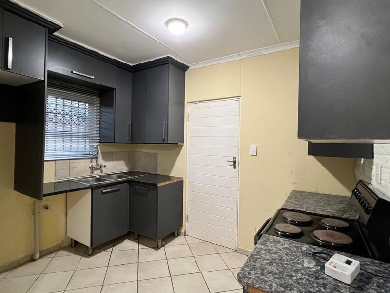 A functional kitchen featuring dark grey cabinetry, laminate countertops, a stainless steel double sink, and an electric hob with tiled flooring.