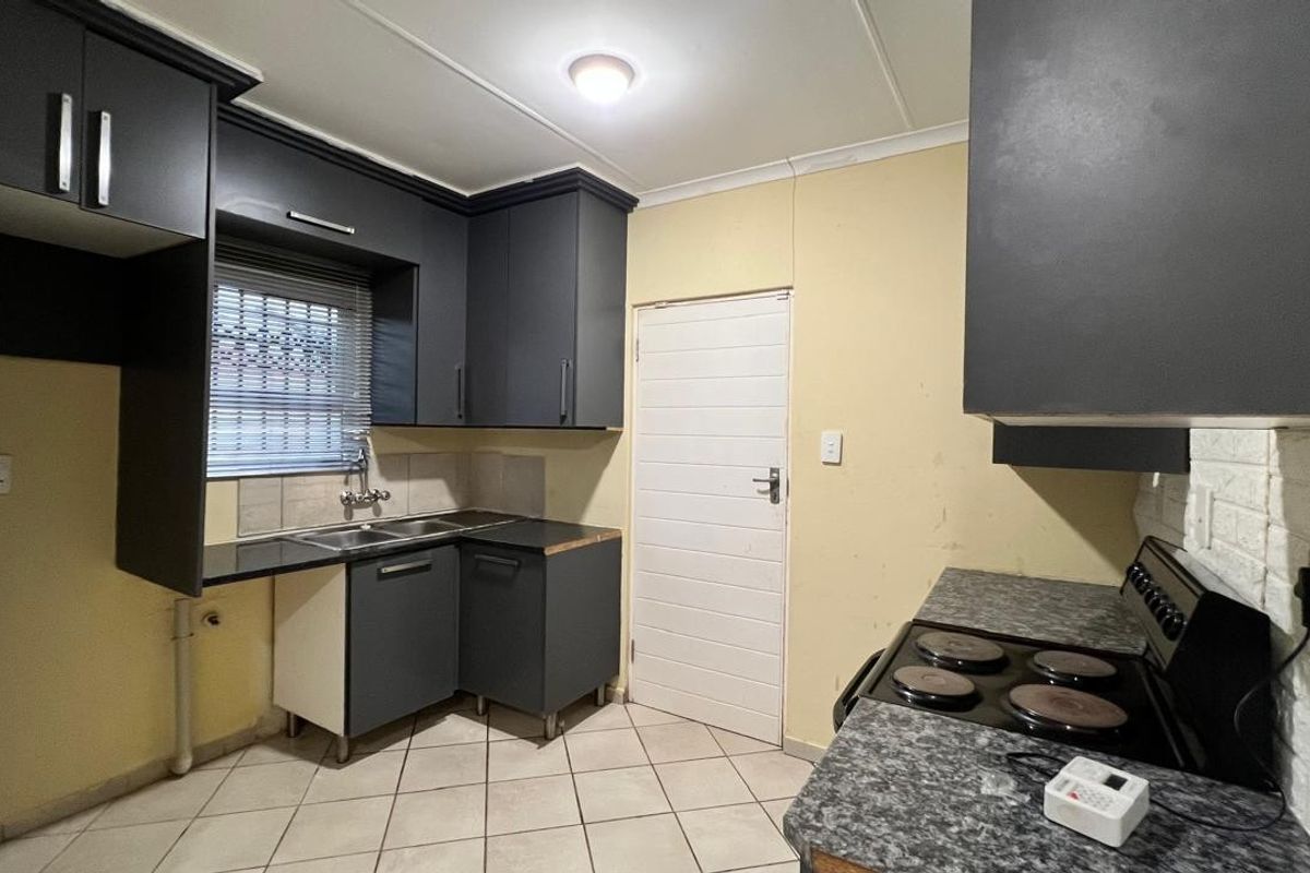A functional kitchen featuring dark grey cabinetry, laminate countertops, a stainless steel double sink, and an electric hob with tiled flooring.