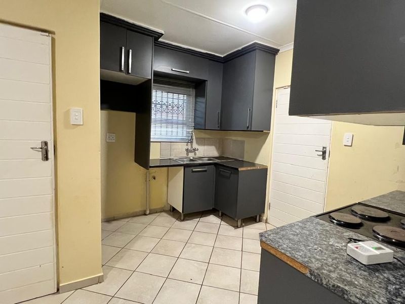 A compact kitchen featuring dark grey cabinetry, laminate countertops, an electric hob, and tiled flooring, offering a functional layout ready for updates.