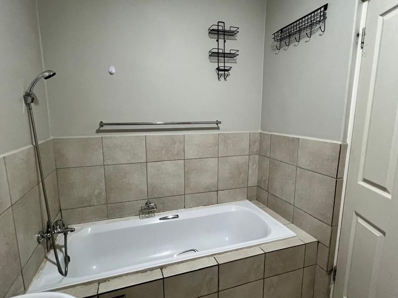 A functional bathroom featuring a built-in bathtub with tiled surround and a handheld shower fixture.