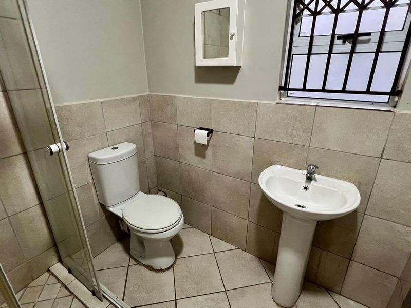 A functional bathroom featuring a pedestal basin, toilet, and a glass-enclosed shower with neutral ceramic tiling throughout.