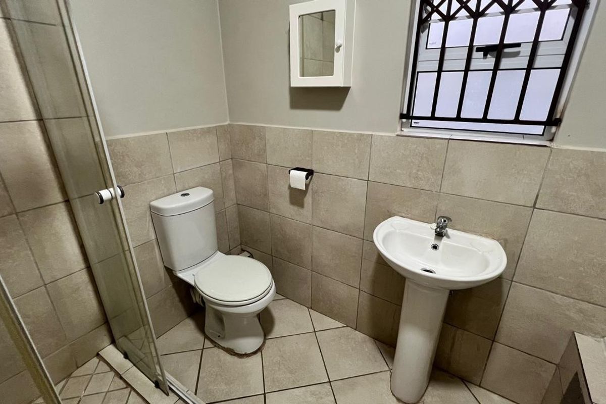 A functional bathroom featuring a pedestal basin, toilet, and a glass-enclosed shower with neutral ceramic tiling throughout.