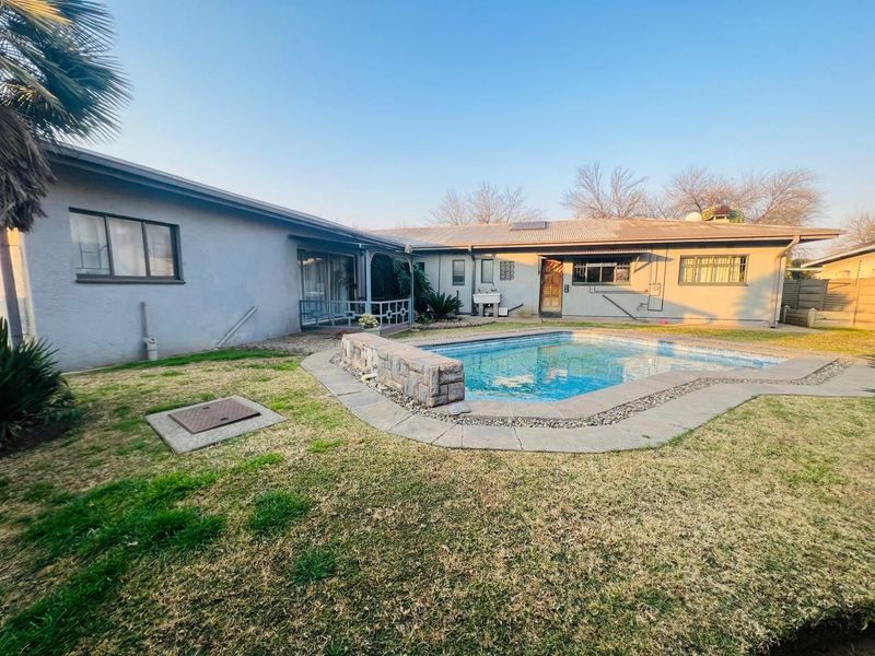 Rear garden area featuring a swimming pool with stone surround, retaining wall, and exterior utility sink against the house facade.