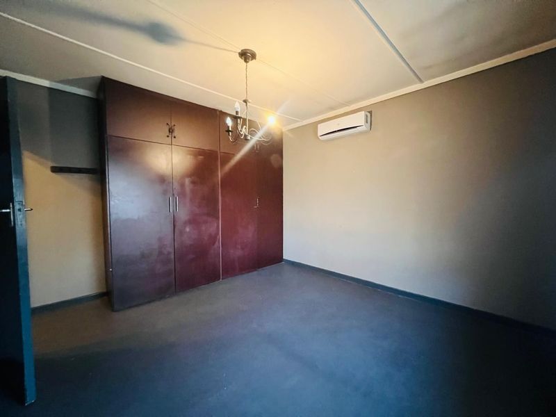 An empty bedroom featuring built-in cupboards, a split-system air conditioner, and a central light fixture.