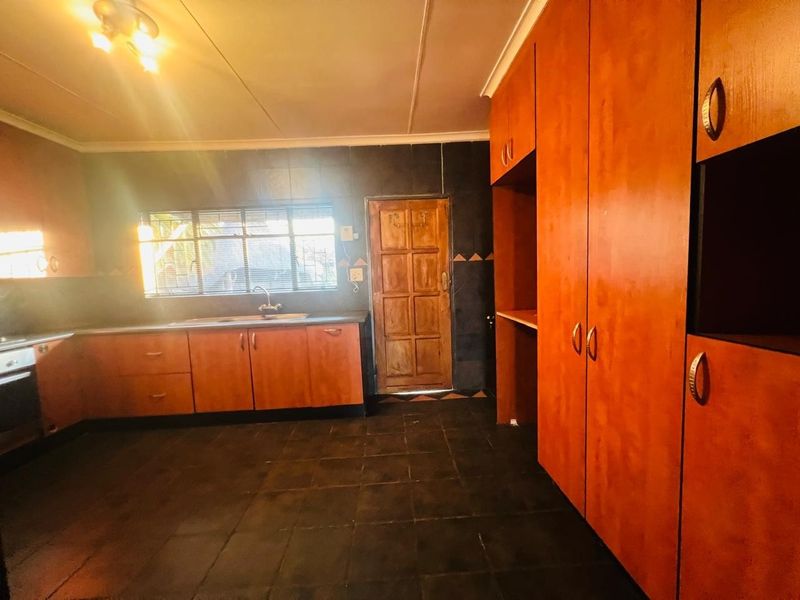 A spacious kitchen featuring extensive wooden cabinetry, built-in oven and hob, dark tiled flooring, and a functional layout with direct exterior access.