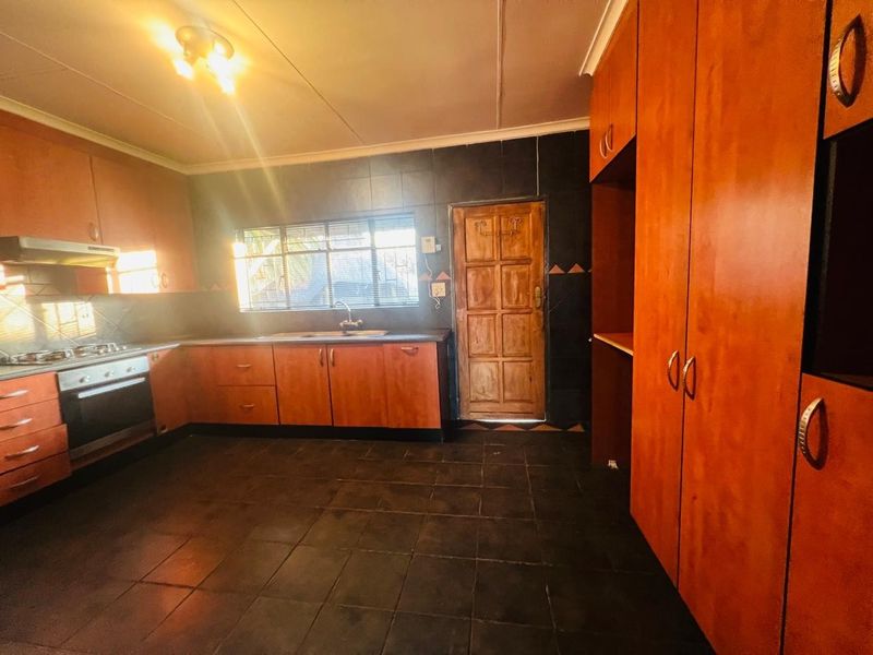 A functional kitchen featuring wooden cabinetry, built-in oven and hob, dark tiled flooring, and a rear access door.