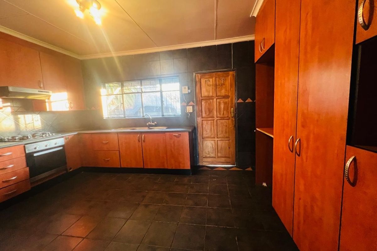 A functional kitchen featuring wooden cabinetry, built-in oven and hob, dark tiled flooring, and a rear access door.