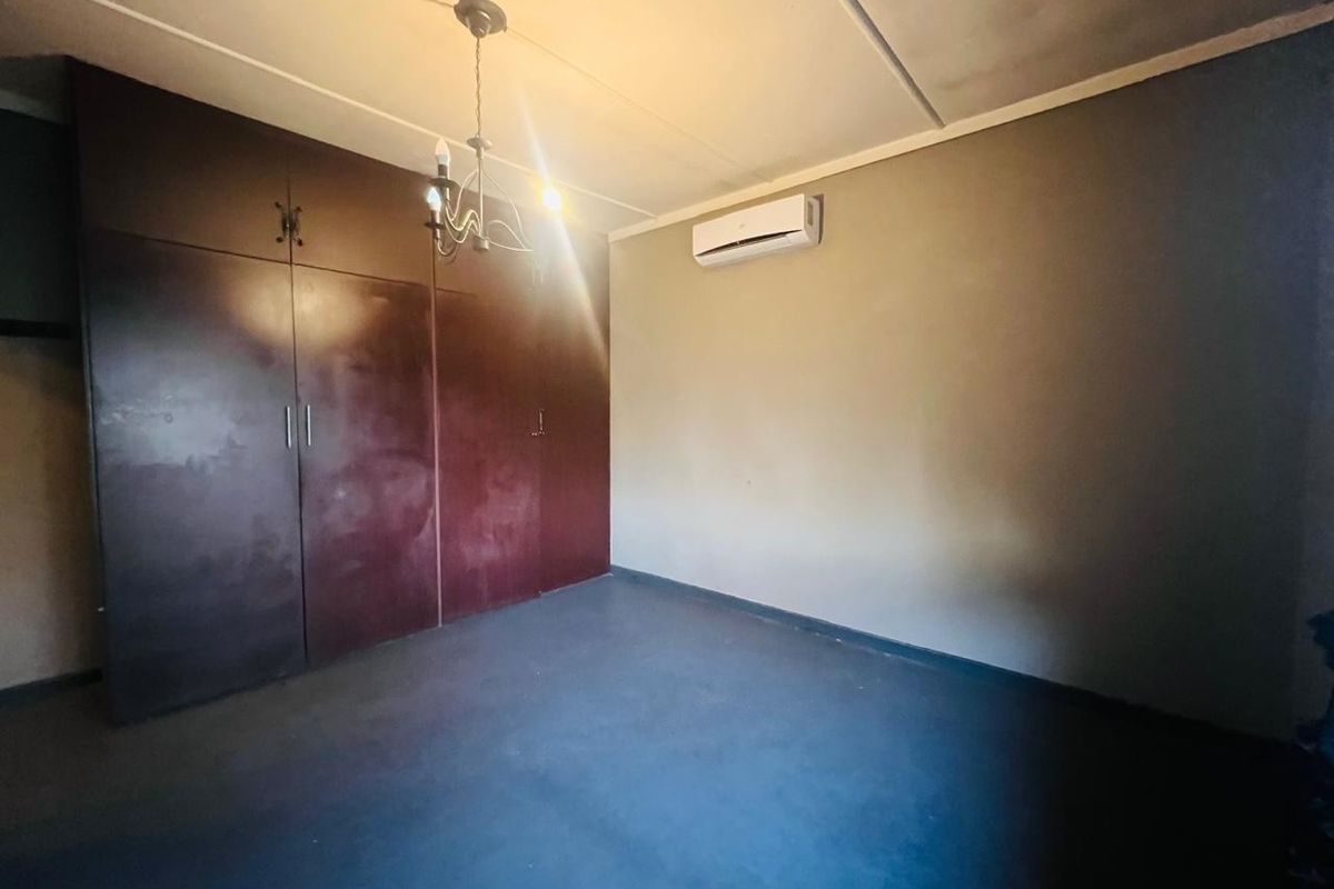 An empty bedroom featuring built-in cupboards, a wall-mounted air conditioning unit, and a central light fixture.