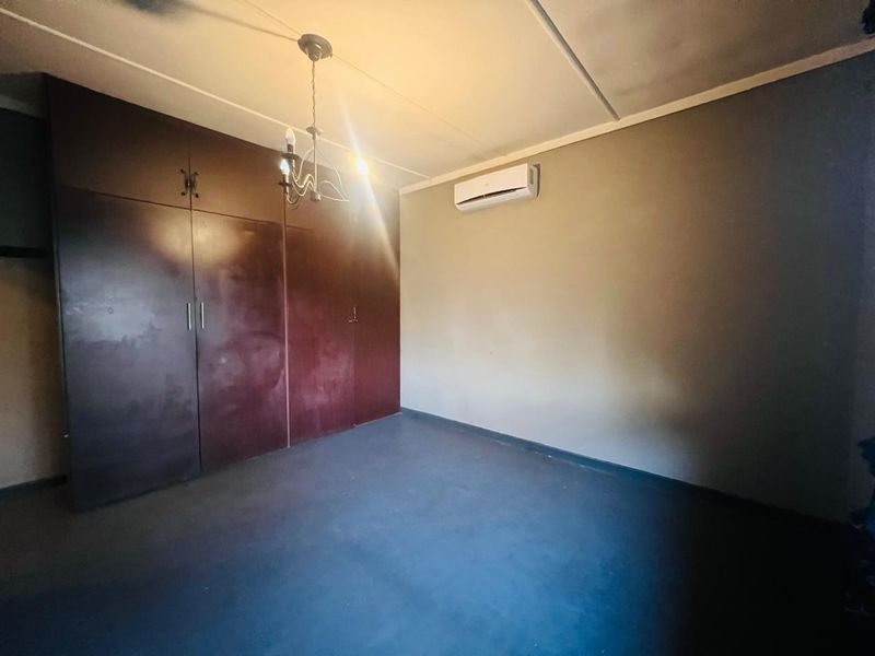 An empty bedroom featuring built-in cupboards, a wall-mounted air conditioning unit, and a central light fixture.