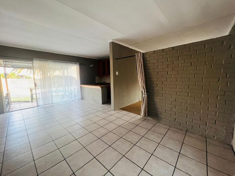 An open-plan living and kitchen area featuring tiled flooring, an exposed brick feature wall, and a sliding glass door leading to the exterior.