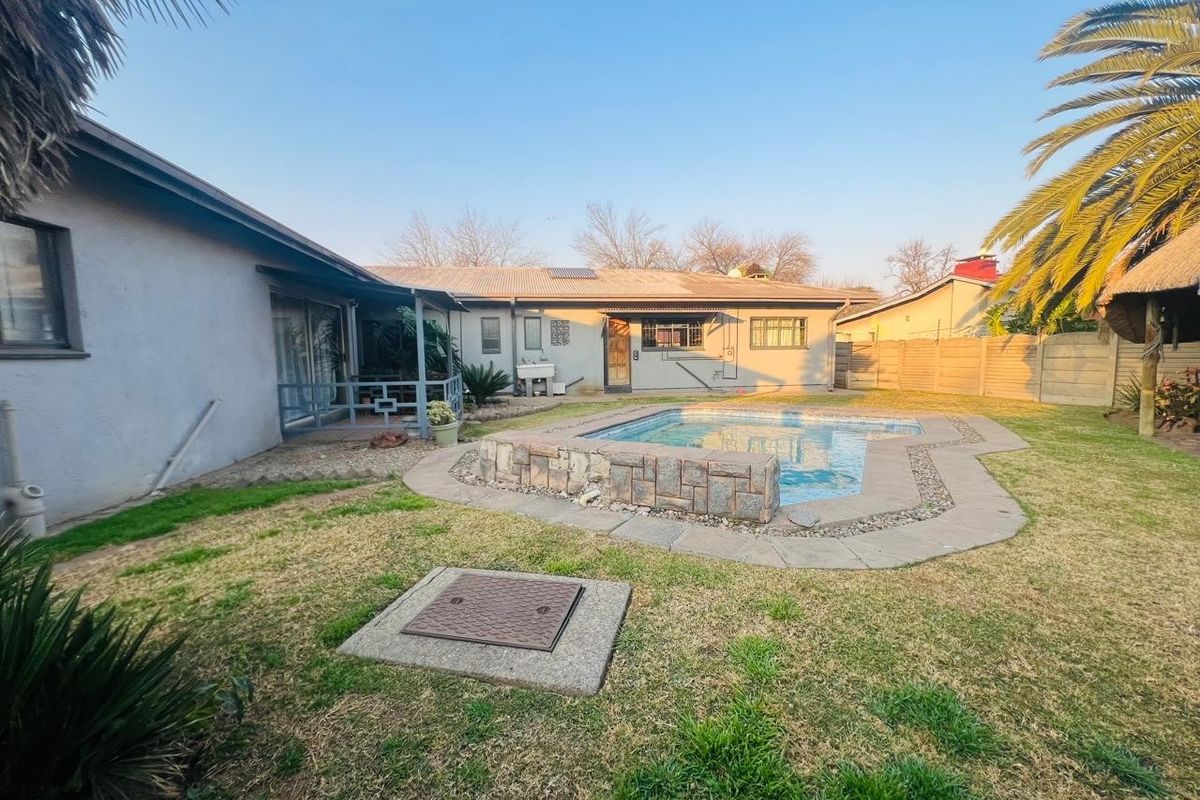 Rear exterior view featuring a swimming pool with stone-clad surround, a covered patio area, and a spacious garden with boundary walling.