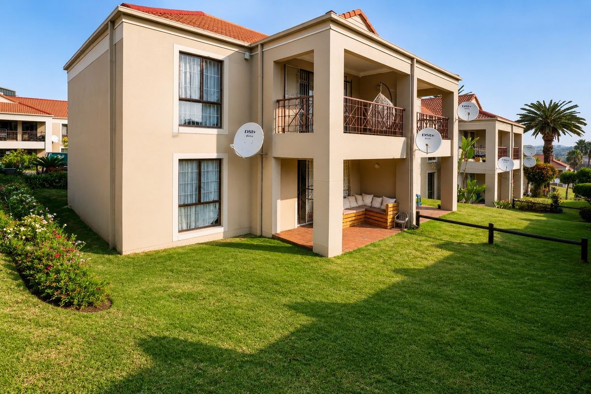 Rear view of a multi-story apartment building featuring covered ground-floor patios, upper-level balconies with metal railings, and well-maintained surrounding lawn areas.