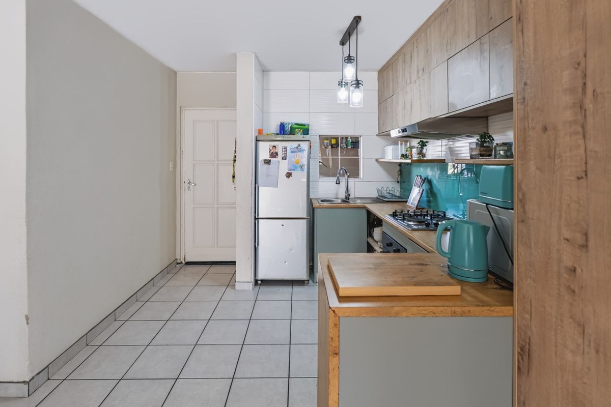 A functional kitchen featuring wood-look cabinetry, a gas hob with extractor fan, tiled backsplash, and neutral floor tiles, offering a practical workspace.