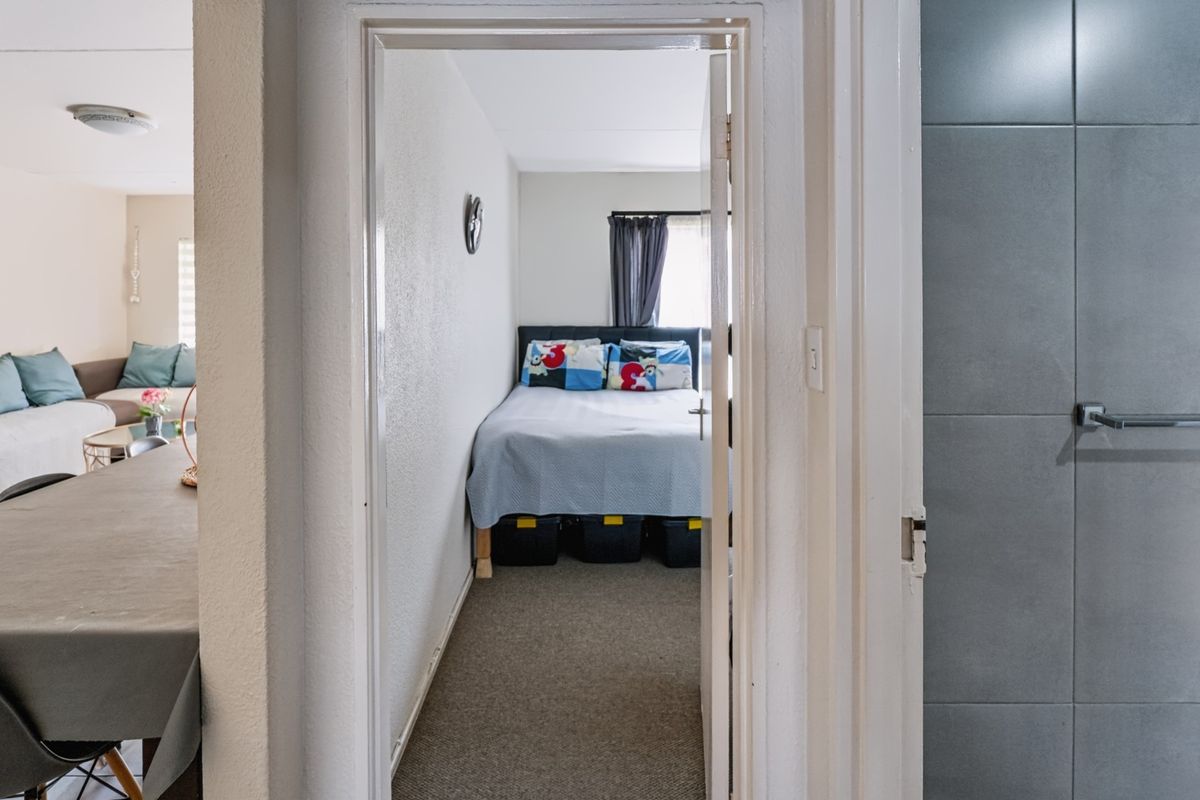 A view through a doorway into a compact bedroom featuring carpeted flooring, adjacent to a tiled bathroom area and living space.