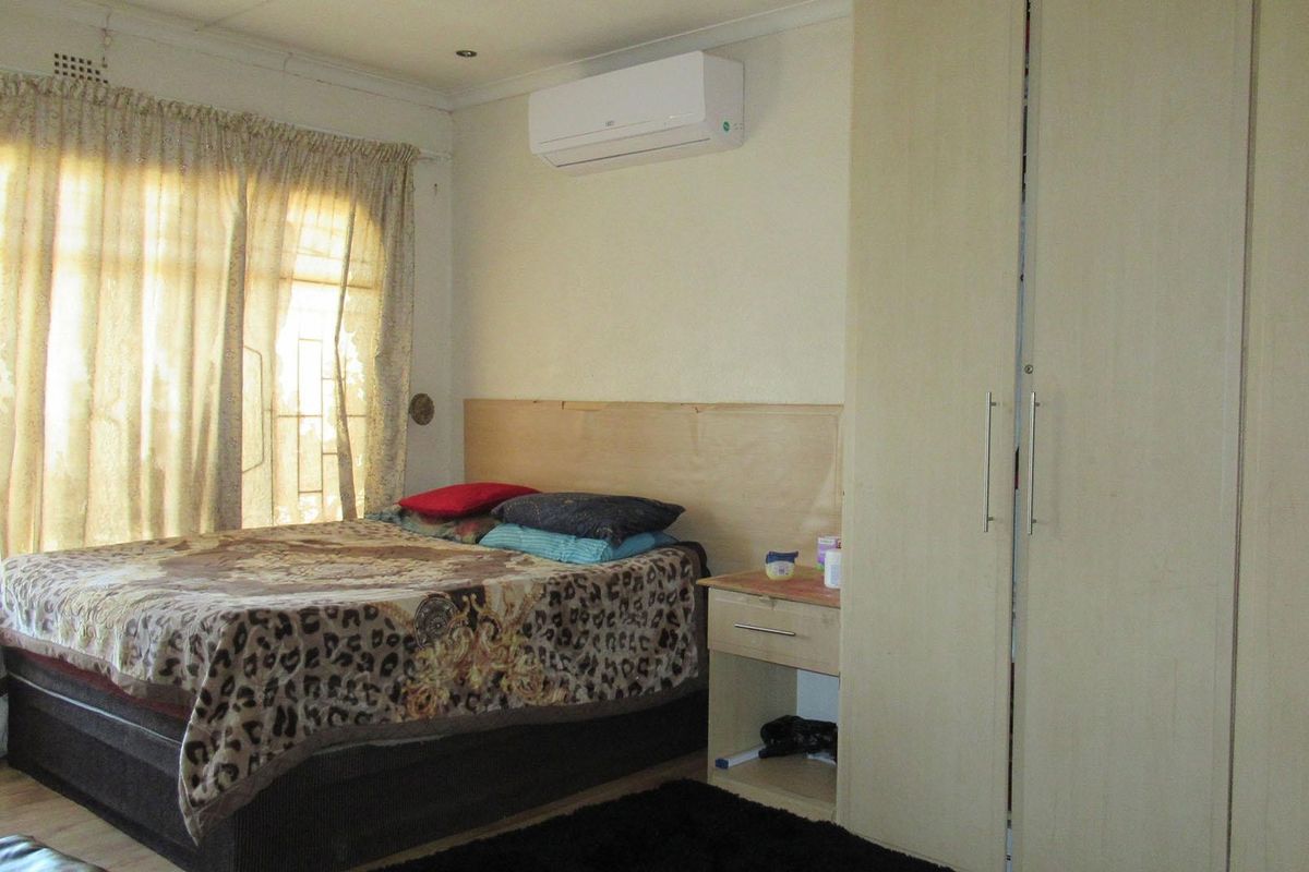 A functional bedroom featuring built-in wardrobes, a wall-mounted air conditioning unit, and laminate flooring with natural light access.