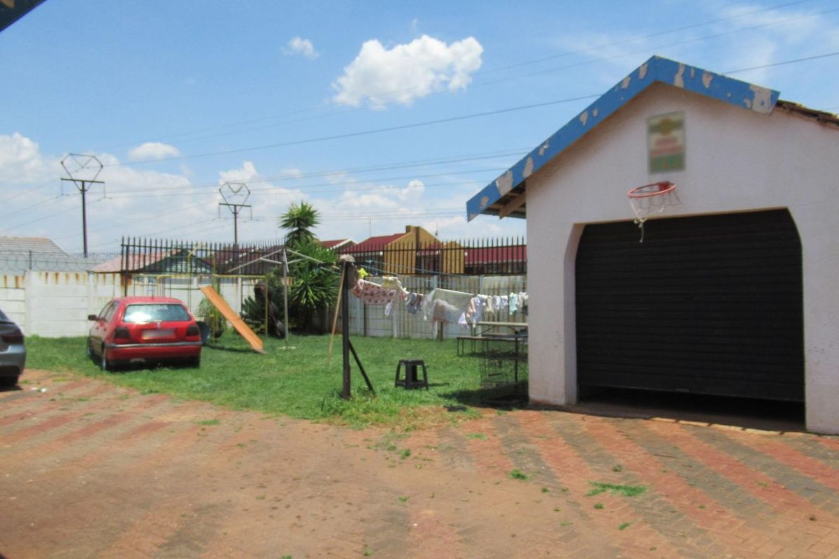 Rear exterior view featuring a detached garage with a roller shutter door, paved driveway area, and perimeter walling with security fencing.