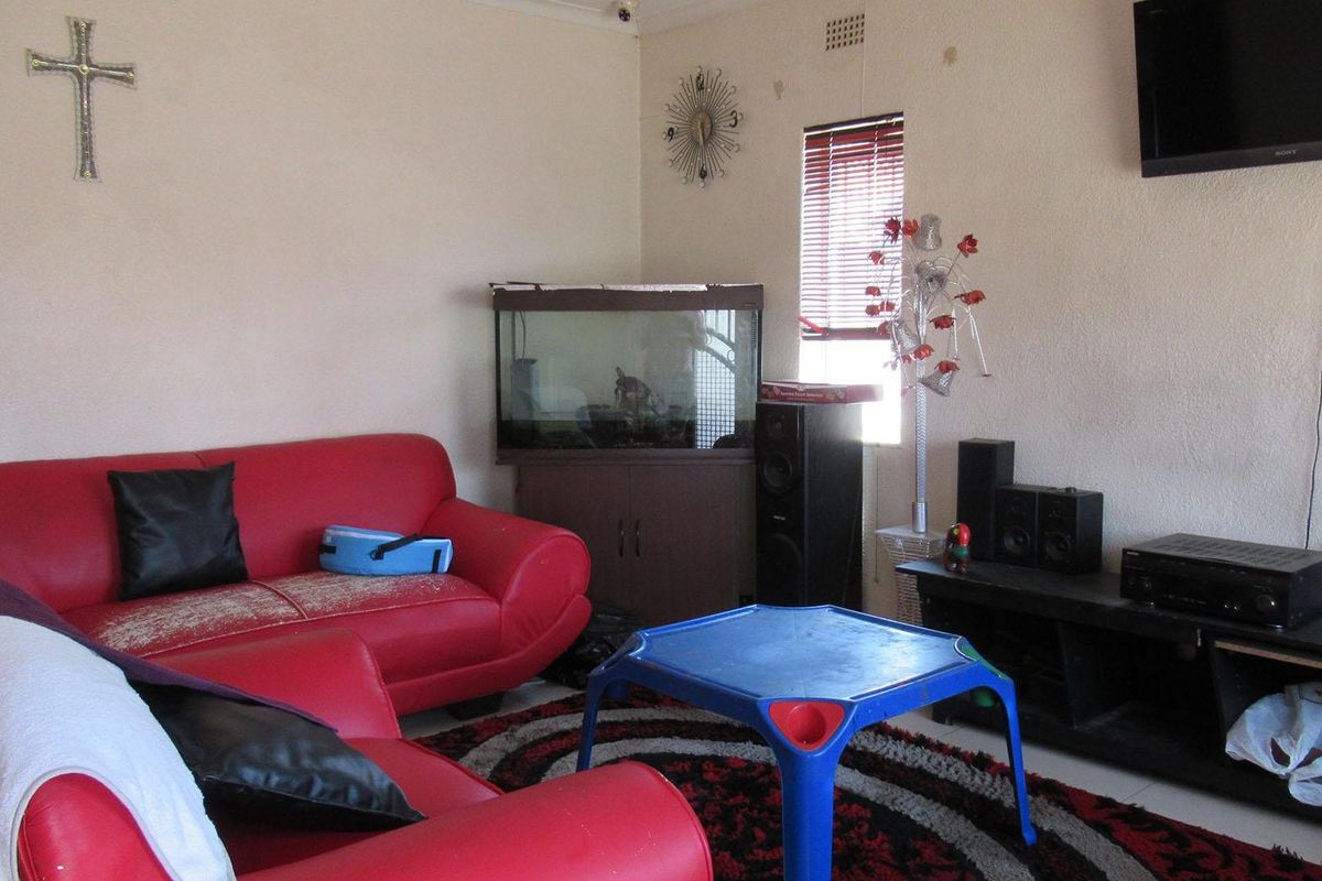 A living room space featuring wall-mounted television and venetian blinds, requiring cosmetic updates to wall finishes to improve the overall aesthetic.