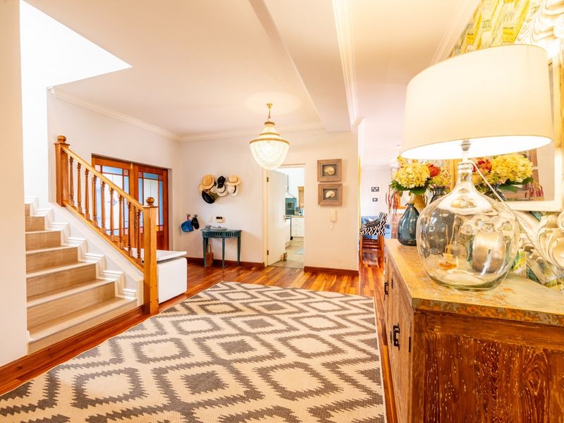 Welcoming entrance hall featuring polished hardwood flooring, a grand timber staircase with a classic balustrade, and an elegant crystal chandelier.