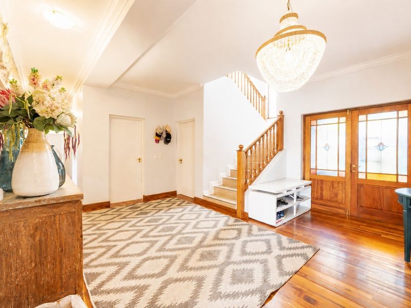 Spacious entrance hall featuring polished hardwood flooring, a grand timber staircase with balustrade, and elegant double front doors with stained glass detailing.