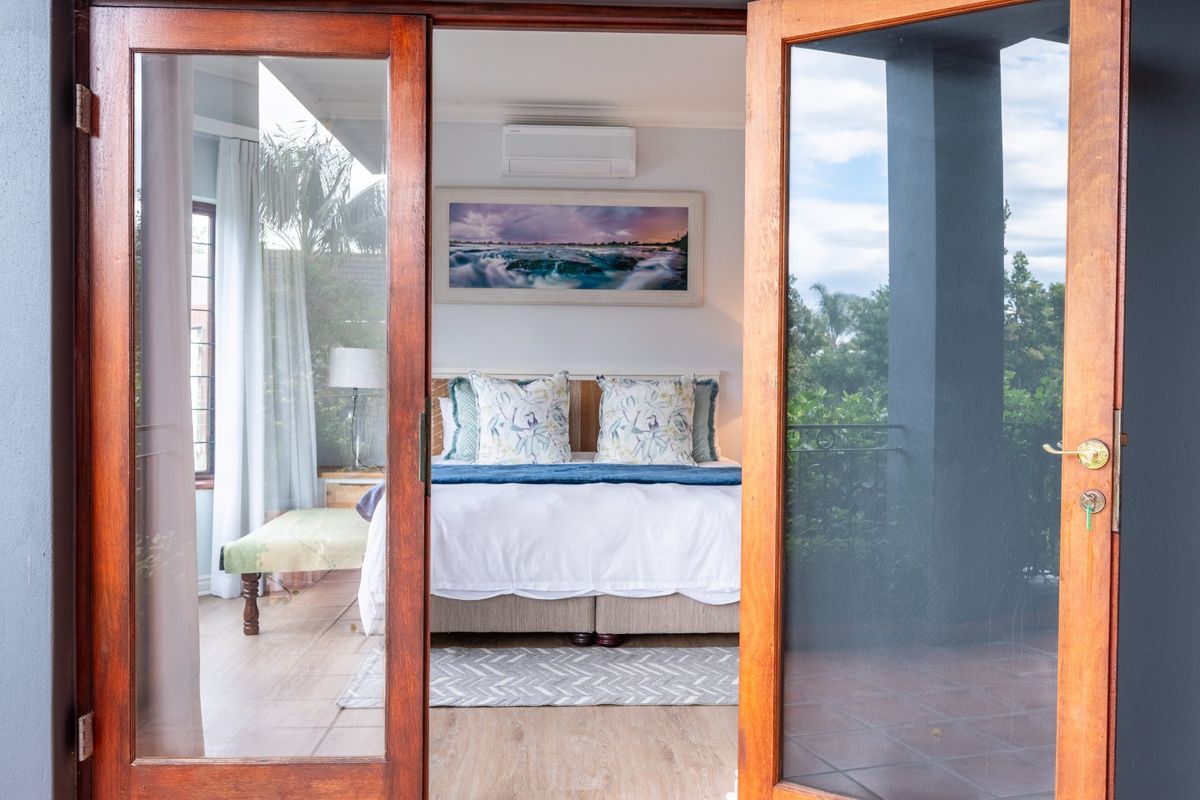 A well-maintained bedroom featuring timber-framed glass doors opening onto a patio, equipped with a split-system air conditioner and neutral tiled flooring.