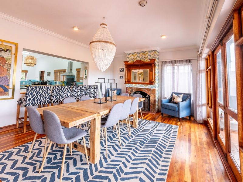 Spacious open-plan dining area featuring polished hardwood floors, a character fireplace, and large timber-framed doors opening to the exterior.