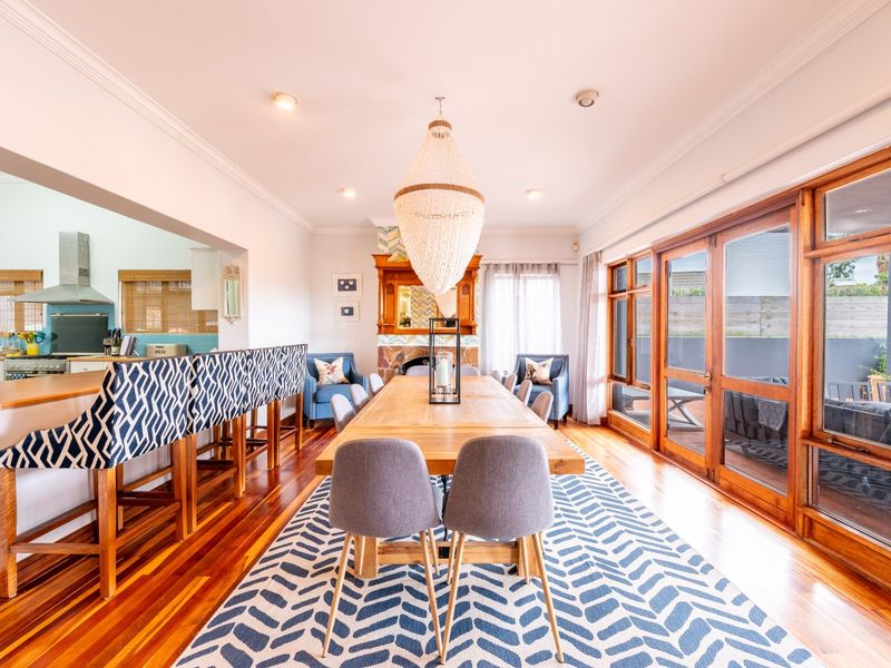 Spacious open-plan dining and kitchen area featuring polished hardwood floors, a fireplace, and large timber-framed glass doors opening to the outdoor space.