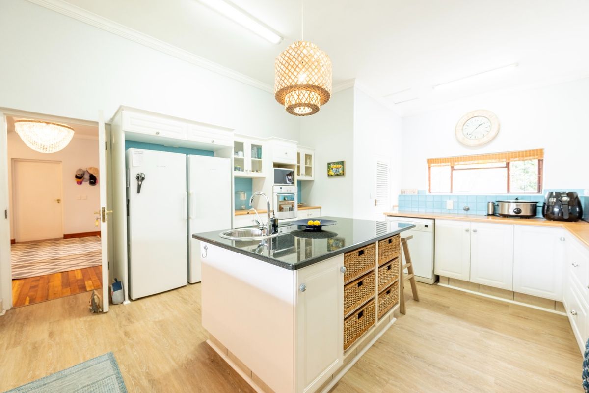 A bright kitchen featuring a central island with a granite countertop, built-in appliances, ample cabinetry, and a light-toned tiled backsplash.