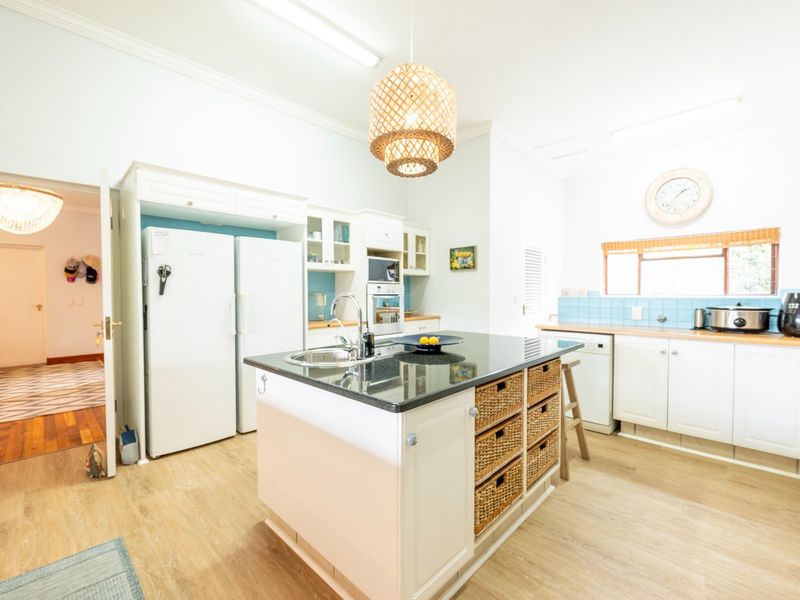 A bright kitchen featuring a central island with a granite countertop, built-in appliances, ample cabinetry, and a light-toned tiled backsplash.