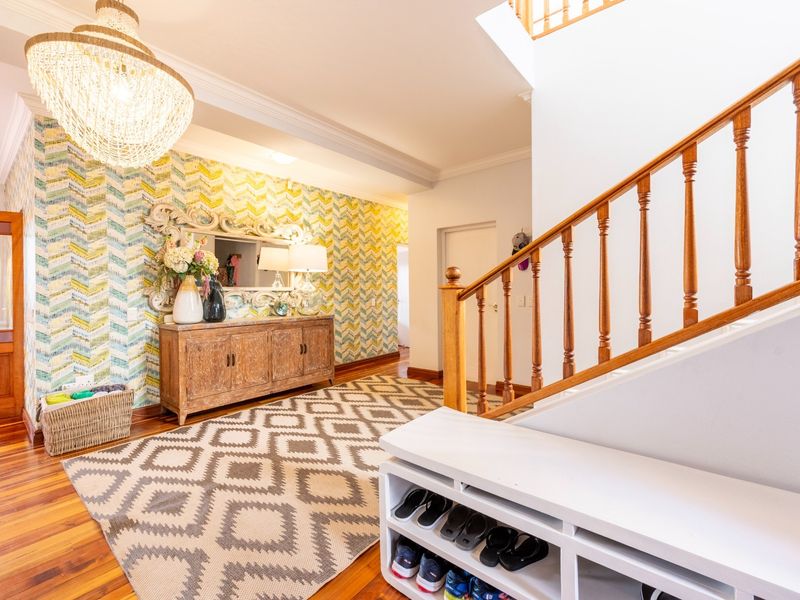 Welcoming entrance hall featuring polished hardwood flooring, a classic timber staircase with balustrade, and decorative feature wallpaper.