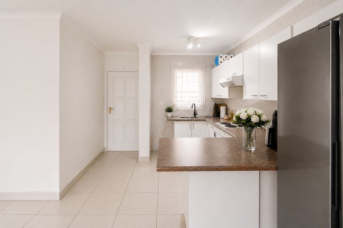 A clean and functional kitchen featuring white cabinetry, laminate countertops, a stainless steel sink, and integrated cooking appliances with tiled flooring.