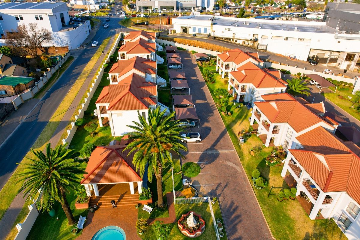 Aerial view of a residential apartment complex featuring tiled roof units, paved driveways, carports, landscaped gardens, and a communal swimming pool.