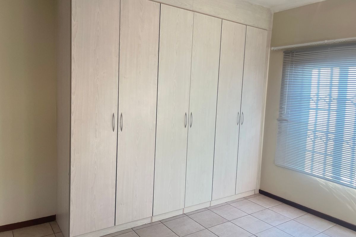 A bright bedroom featuring extensive built-in cupboards, neutral tiled flooring, and fitted venetian blinds.