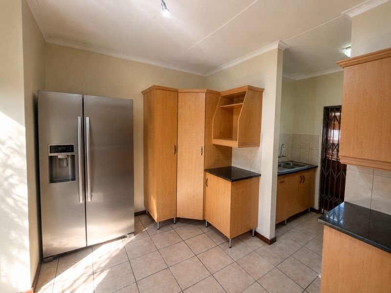 A functional scullery area featuring built-in wooden cabinetry, granite countertops, a stainless steel sink, and tiled flooring with access to an exterior security gate.