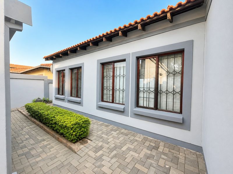 A well-maintained rear exterior view featuring a paved walkway, neat landscaping, and a classic tiled roof with exposed timber rafters.