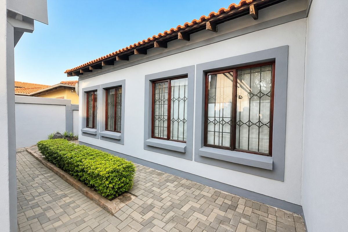 A well-maintained rear exterior view featuring a paved walkway, neat landscaping, and a classic tiled roof with exposed timber rafters.