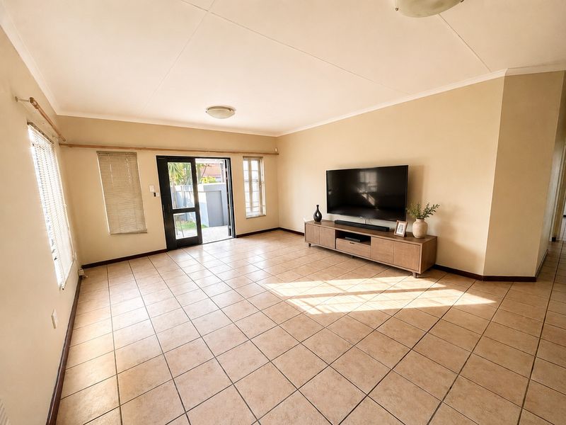 A spacious living room featuring neutral tiled flooring, large windows with blinds, and a sliding glass door providing direct access to the outdoor area.