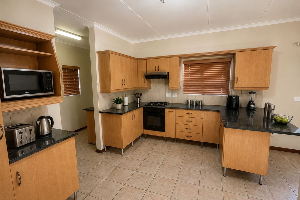 A functional kitchen featuring light wood cabinetry, granite countertops, a gas hob, built-in oven, and tiled flooring with a pass-through to a secondary area.